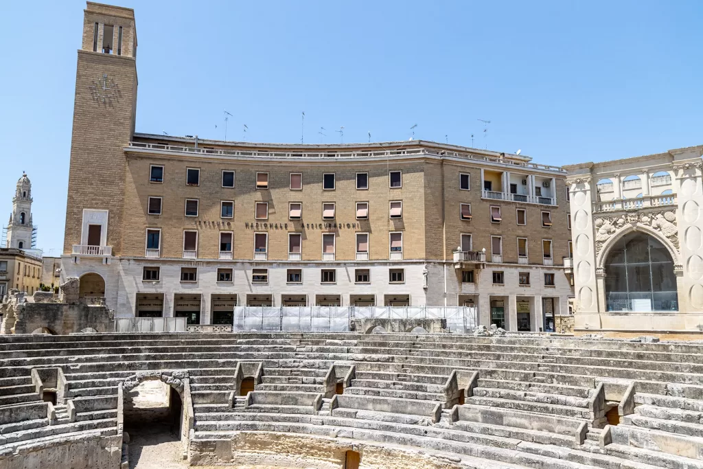 I resti dell'anfiteatro di Lecce con il sedile e il palazzo razionalista